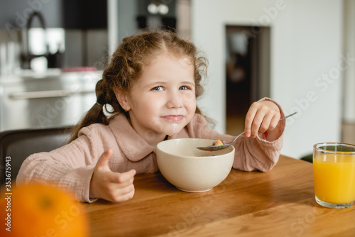 selective focus of kid holding spoon near bowl with corn flakes and glass of orange juice