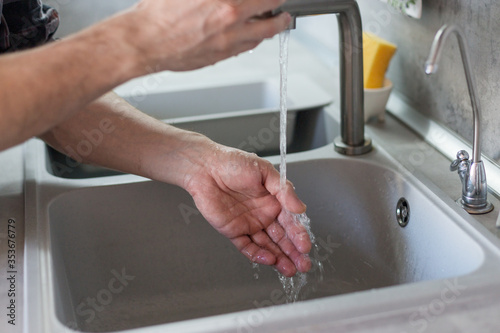 Man washes his hands in the kitchen under the tap close up