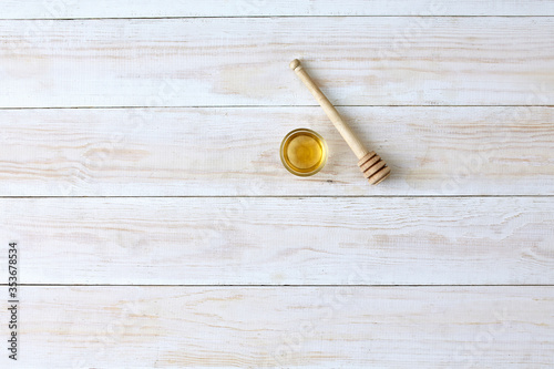 small honey bowl with wooden honey spoon on wooden background, top view