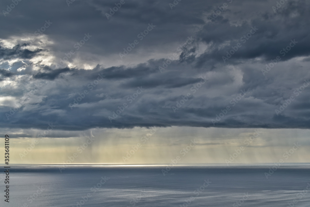 Sun shines through rain clouds over Tasman sea horizon