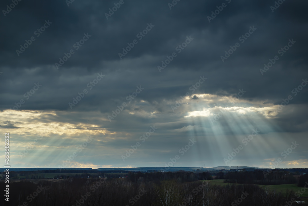 The sun's rays break through the clouds over the fields. Before the storm.