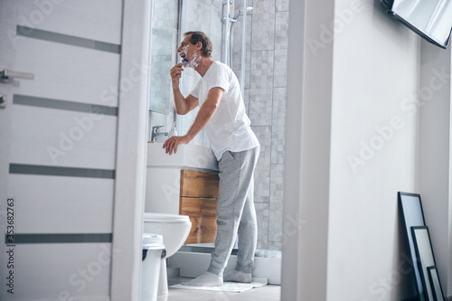 Concentrated male with an open mouth shaving his face