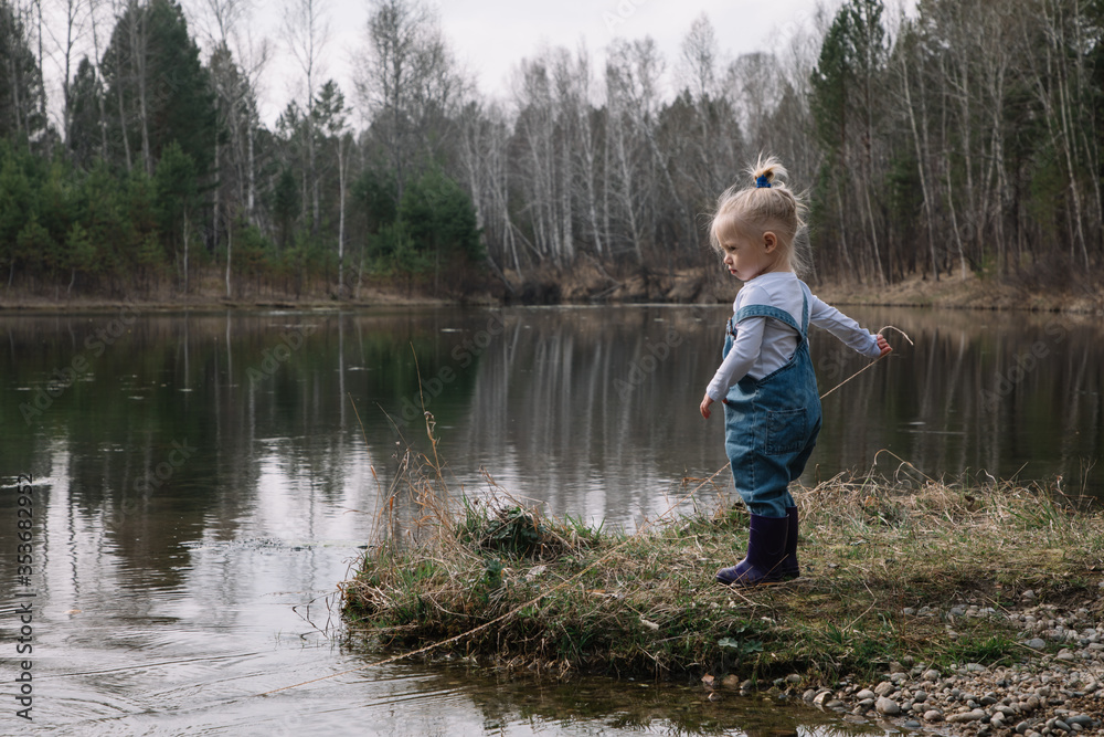 Little girl in rubber boots catches and feeds fish on the river in a jar