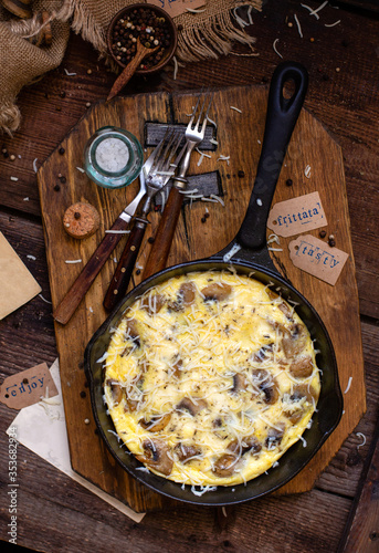 overhead shot of tasty fried eggs breakfast (omelette, scrambled eggs, frittata) with mushrooms and cheese in cast iron pan on rustic wooden board and table