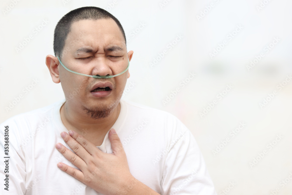 Fototapeta premium Asian man having asthma and hard to breathing while his hand touching chest. Covid-19 patient in hospital suffer from respiratory disorder with oxygen tubing on his nose