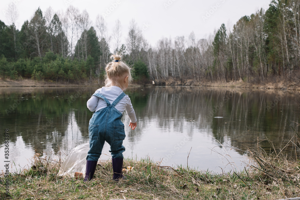 Little girl in rubber boots catches and feeds fish on the river in a jar Little girl in rubber boots catches and feeds fish on the river in a jar