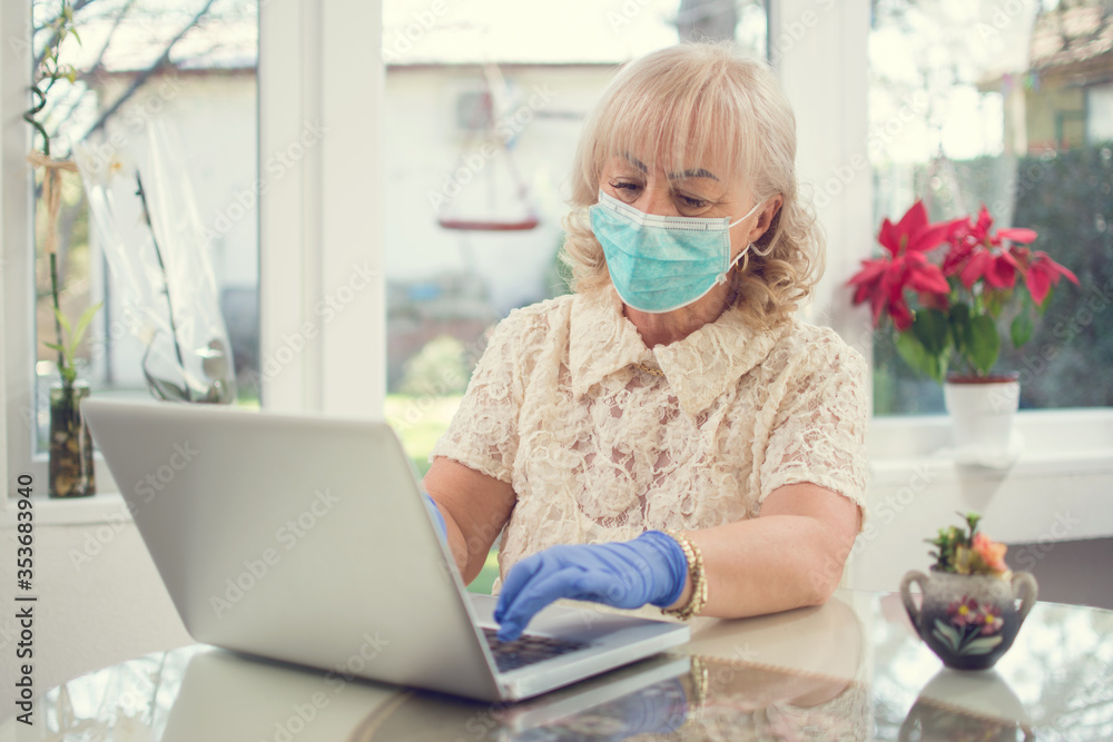 Senior woman wearing protective mask and gloves using laptop at home. Covid-19 (Coronavirus), quarantine, seniors and technology concept.