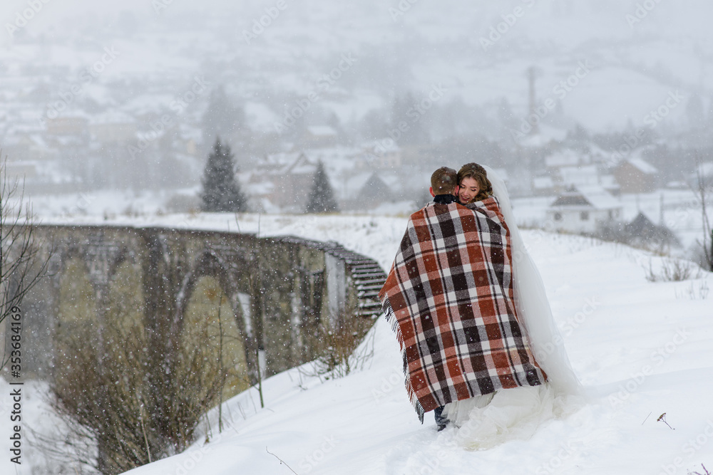The bride and groom cuddle under a rug to keep warm. Winter wedding
