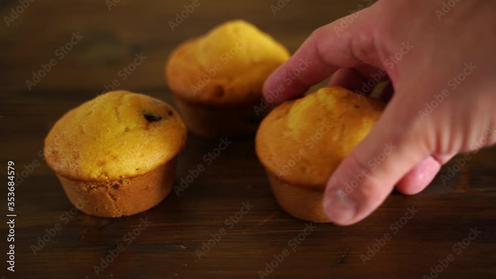 three homemade cupcakes lying on a wooden Board. A hand takes one and carries out three homemade cupcakes lying on a wooden Board. A hand takes one and carries out