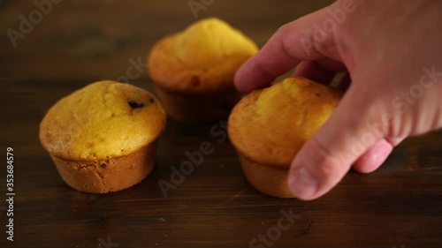 three homemade cupcakes lying on a wooden Board. A hand takes one and carries out
