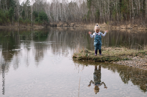 Little girl in rubber boots catches and feeds fish on the river in a jar