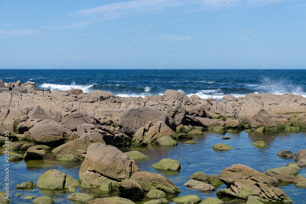 ocean wave splash on rocks on the coast on a sunny day with blue sky