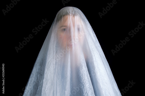The contour of the face of a young woman under transparent film. Ghost on black background.
