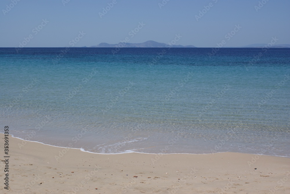 A quiet Mediterranean beach on the Greek island of Donoussa on a summers day.  The horizon in the distance with crystal clear blue sea waters lapping onto a pristine beach.  Copy space.