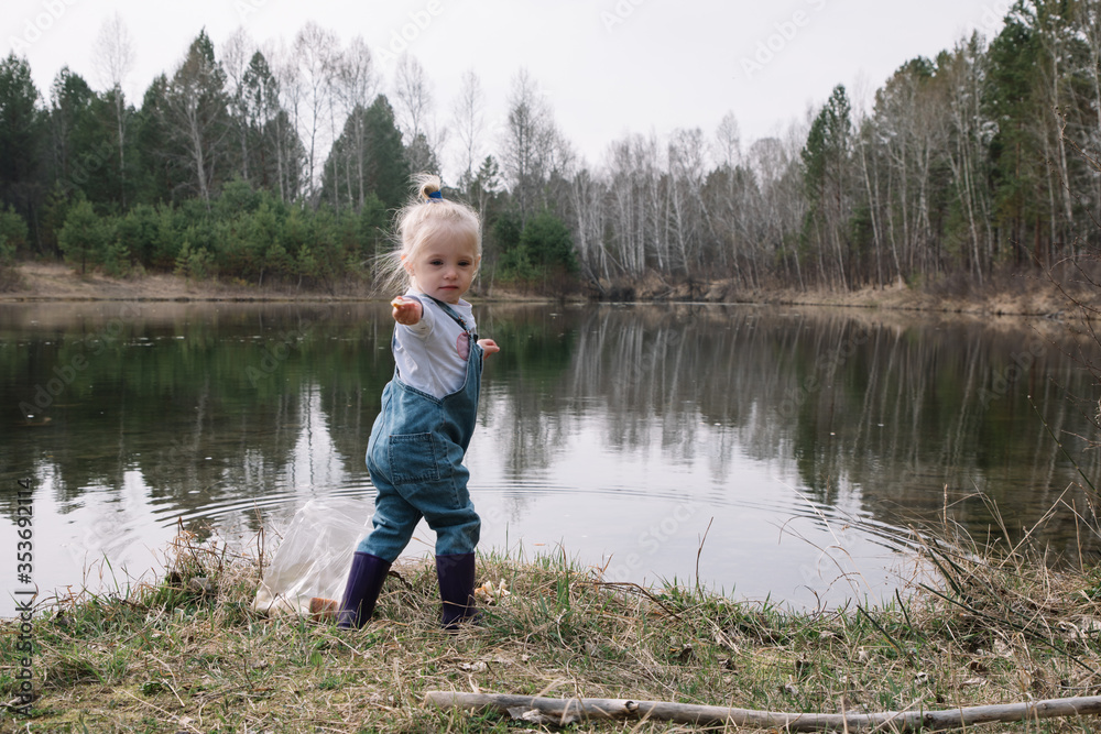 Little girl in rubber boots catches and feeds fish on the river in a jar Little girl in rubber boots catches and feeds fish on the river in a jar
