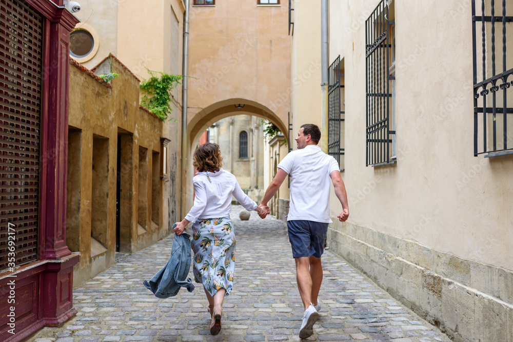 Loving couple walks by the hand. The couple runs their backs into the frame along a narrow street.