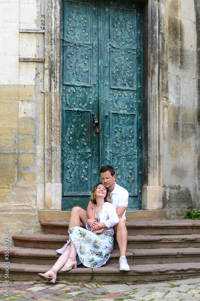 Two lovers are sitting on the steps of an old church. The guy hugs the girl from behind. The couple is happy. Two lovers are sitting on the steps of an old church. The guy hugs the girl from behind. The couple is happy.
