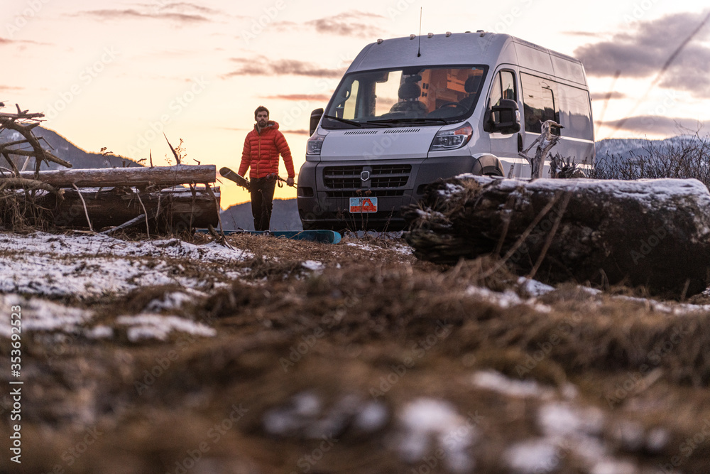 Man by a camper van carrying skis in a rocky wintry landscape. Man by a camper van carrying skis in a rocky wintry landscape.
