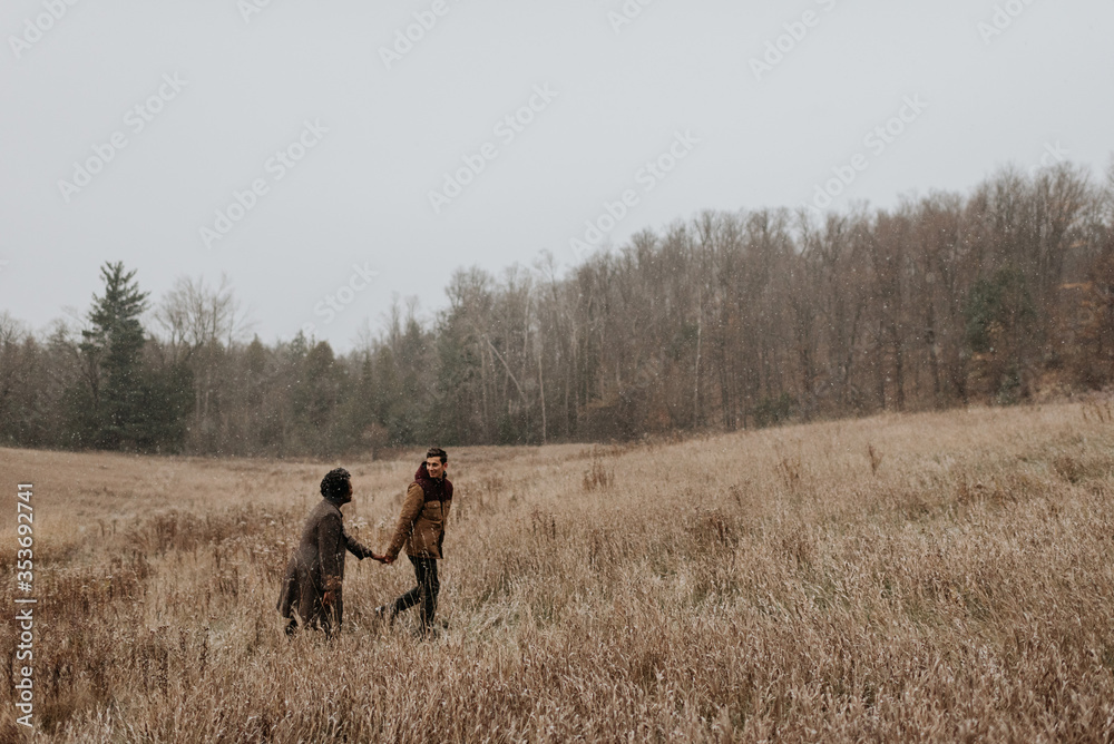 A couple holding hands and looking at each other walking through long grasses in a wintry landscape. A couple holding hands and looking at each other walking through long grasses in a wintry landscape.
