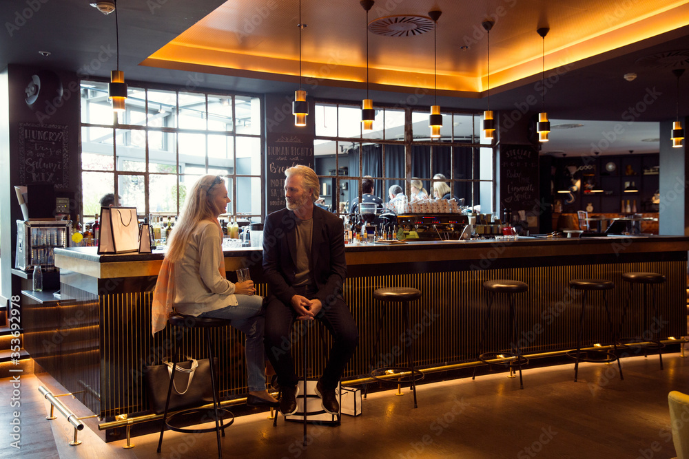 A couple sitting on bar stools next to a bar. A couple sitting on bar stools next to a bar.