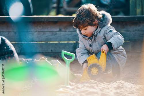 A child in a sandpit with a toy digger and spade. photo