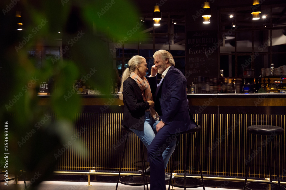 An older couple sitting face to face close to each other at a bar. An older couple sitting face to face close to each other at a bar.
