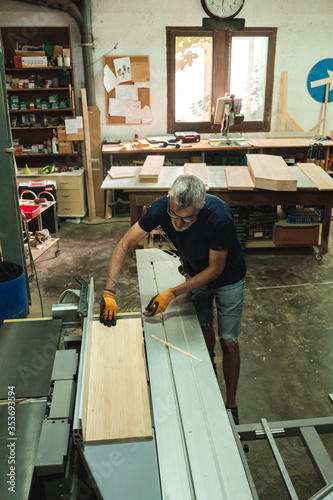 Carpenter cutting a piece of wood on the electric saw cutting machine in a wood workshop