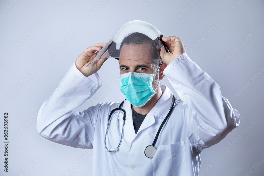 medico in camice bianco e stetofonendoscopio al collo indossa una mascherina chirurgica e una visiera protettiva in plexiglas isolato su sfondo bianco medico in camice bianco e stetofonendoscopio al collo indossa una mascherina chirurgica e una visiera protettiva in plexiglas isolato su sfondo bianco