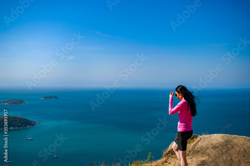 A young women brunette in pink dress watches, enjoys a view from the mountain. Sportswear, cap. The Andamand Sea of Phuket Island, Thailand.