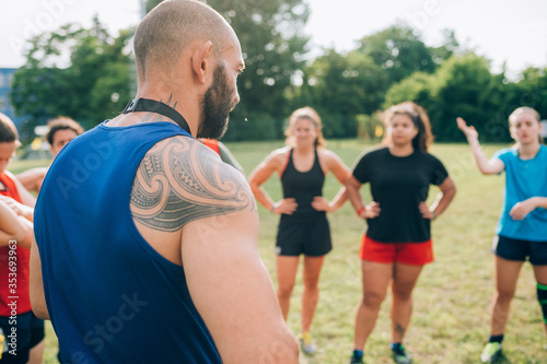 A group of women standing in a circle listening to their male rugby coach.