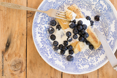 Morning breakfast with french crepes, fresh blueberry, yogurt on a plate on wooden table background. Top view.