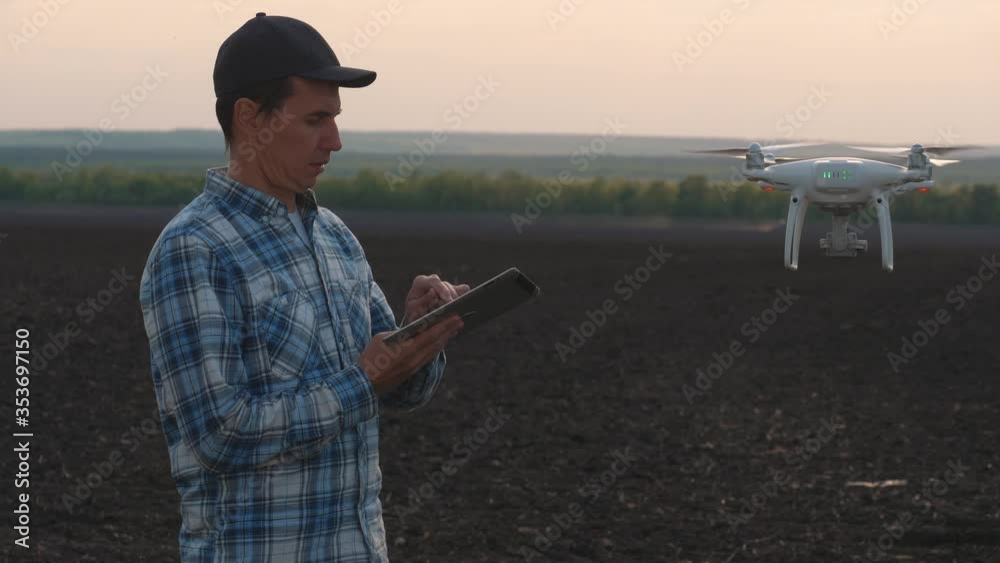 A male farmer stands on a black plowed field and holds a control panel of a drone. The use of smart technology in managing the agricultural process. A male farmer stands on a black plowed field and holds a control panel of a drone. The use of smart technology in managing the agricultural process.