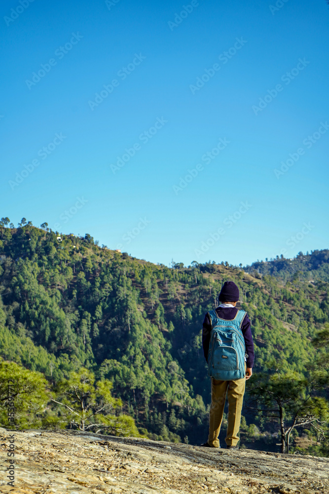 Almora, Uttrakhand / India- May 30 2020 : A school boy standing on the cliff of a mountain with beautiful blue sky overhead.