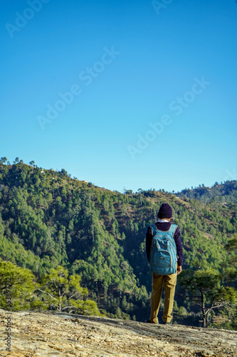 Almora, Uttrakhand / India- May 30 2020 : A school boy standing on the cliff of a mountain with beautiful blue sky overhead.
