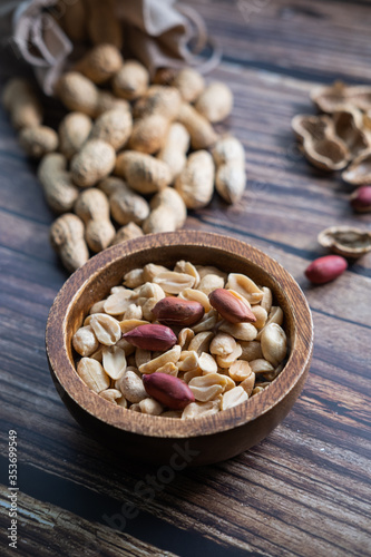 Peanuts in a wooden bowl on wooden background. Healthy snack. Vertical picture.