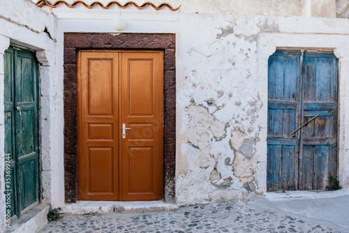 Three old wooden doors in different colors. White stone wall. Traditional village of Pyrgos on Santorini island, Greece. 