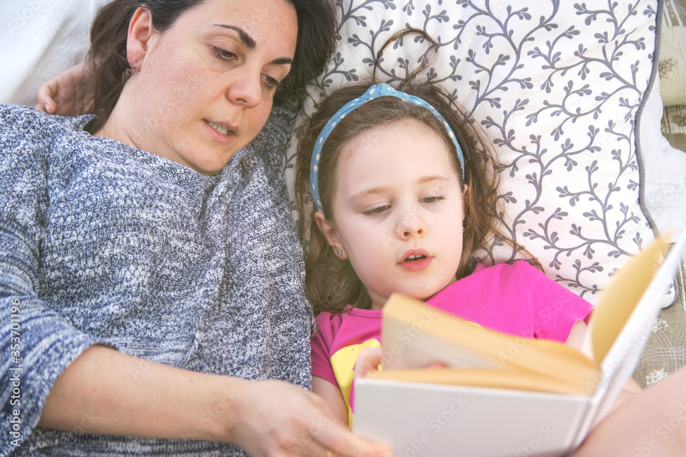 Mother and daughter lying on bed reading a story book. Top-down shoot. Home schooling concept with empty copy space for Editor's text. Mother and daughter lying on bed reading a story book. Top-down shoot. Home schooling concept with empty copy space for Editor's text.