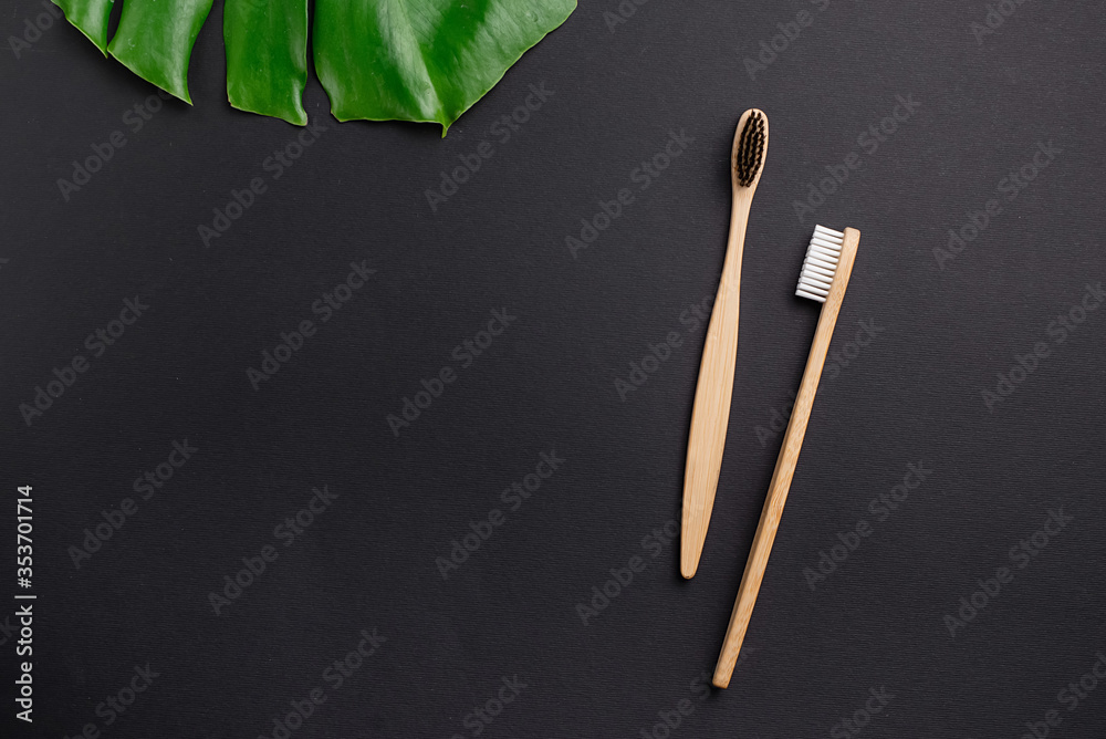 Flat lay composition with two wooden bamboo eco friendly toothbrushes, green leaves monstera and space for text on black background. Teeth hygiene. Top view, copy space Flat lay composition with two wooden bamboo eco friendly toothbrushes, green leaves monstera and space for text on black background. Teeth hygiene. Top view, copy space