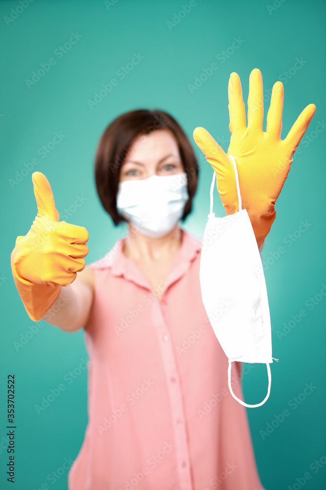 Woman in yellow latex gloves and in a protective medical mask holds in her hands a protective medical mask on a green background Woman in yellow latex gloves and in a protective medical mask holds in her hands a protective medical mask on a green background