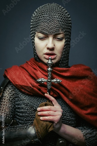 Murais de parede Gorgeous young woman in knight armour and steel chainmaille holding dagger on dark background