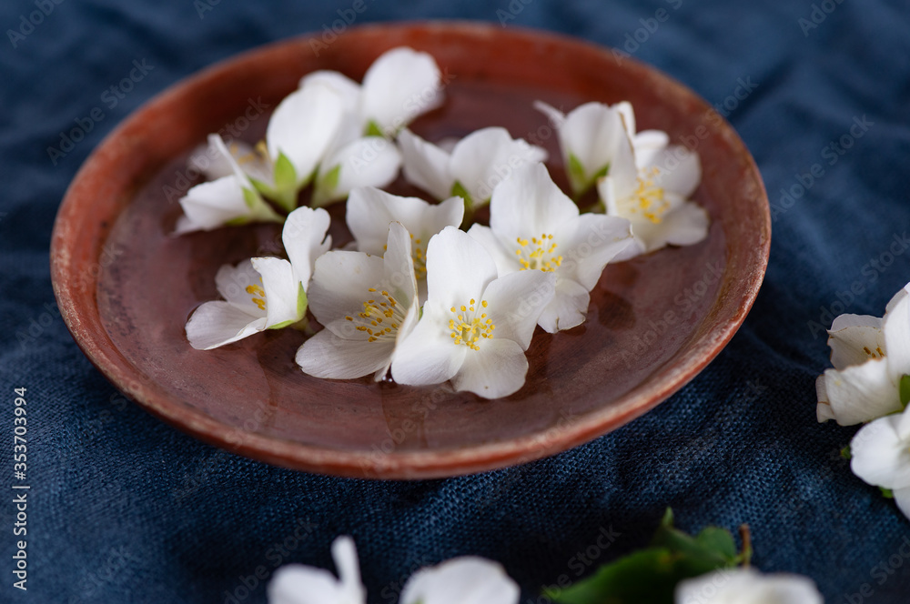 White jasmine flowers, clay plate, on a dark blue textile background