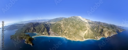 Fototapeta Naklejka Na Ścianę i Meble -  Extreme sport. Landscape .Paragliding in the sky. Paraglider tandem flying over the sea with blue water and mountains in bright sunny day. Aerial view of paraglider and Blue Lagoon in Oludeniz, Turkey