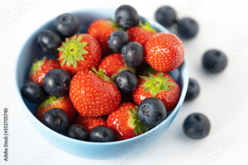 fresh strawberries and blueberries in a blue bowl on a white background close up