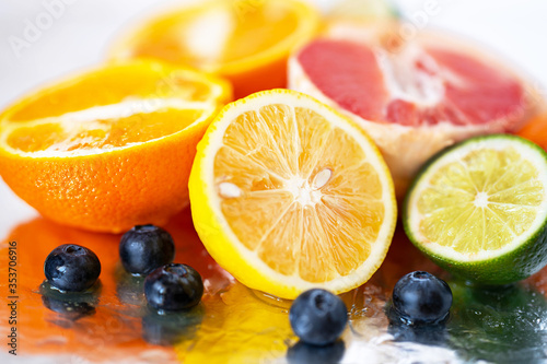 several fresh citrus fruits cut in half  including lemon  orange and lime  and blueberries on a silvery surface