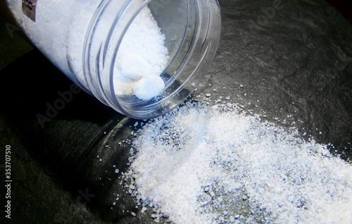 a white handful of salt spilled from a jar on a black stone surface