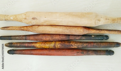 Set of wooden rolling pins with various colours, shapes and sizes on white floor, background.