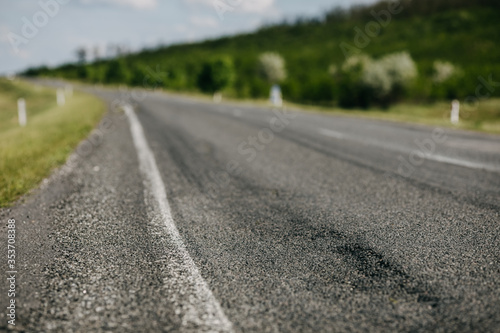 Damaged asphalt road in the countryside with tire marks. Closeup, shallow depth of field.