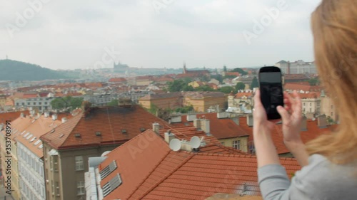 panoramic view on old buildings in Prague from top and girl is taking pictures by smartphone photo