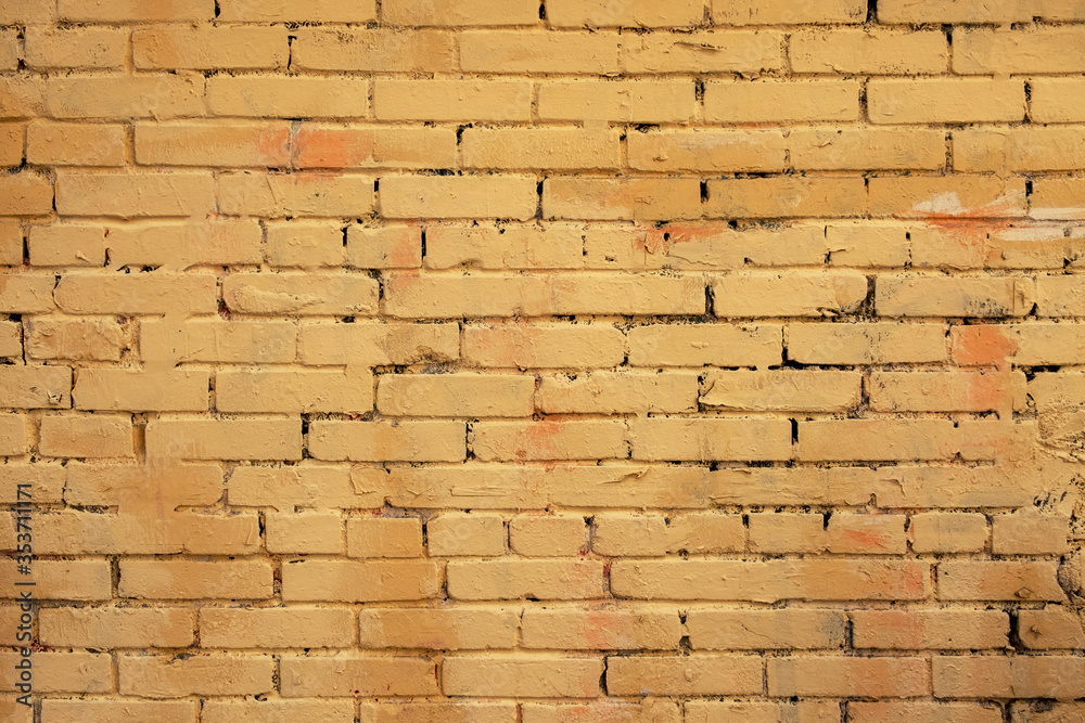 Fototapeta premium old tattered painted yellow brick wall. rough surface texture