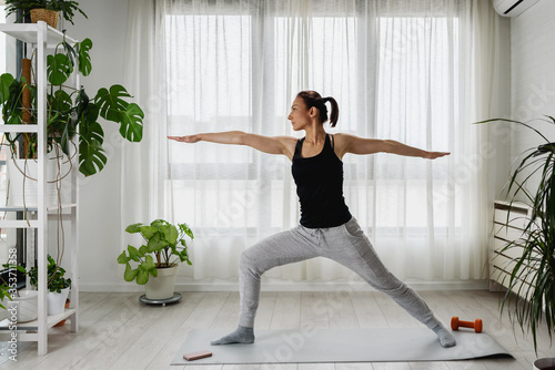 Woman practicing yoga at home in the morning by the big window